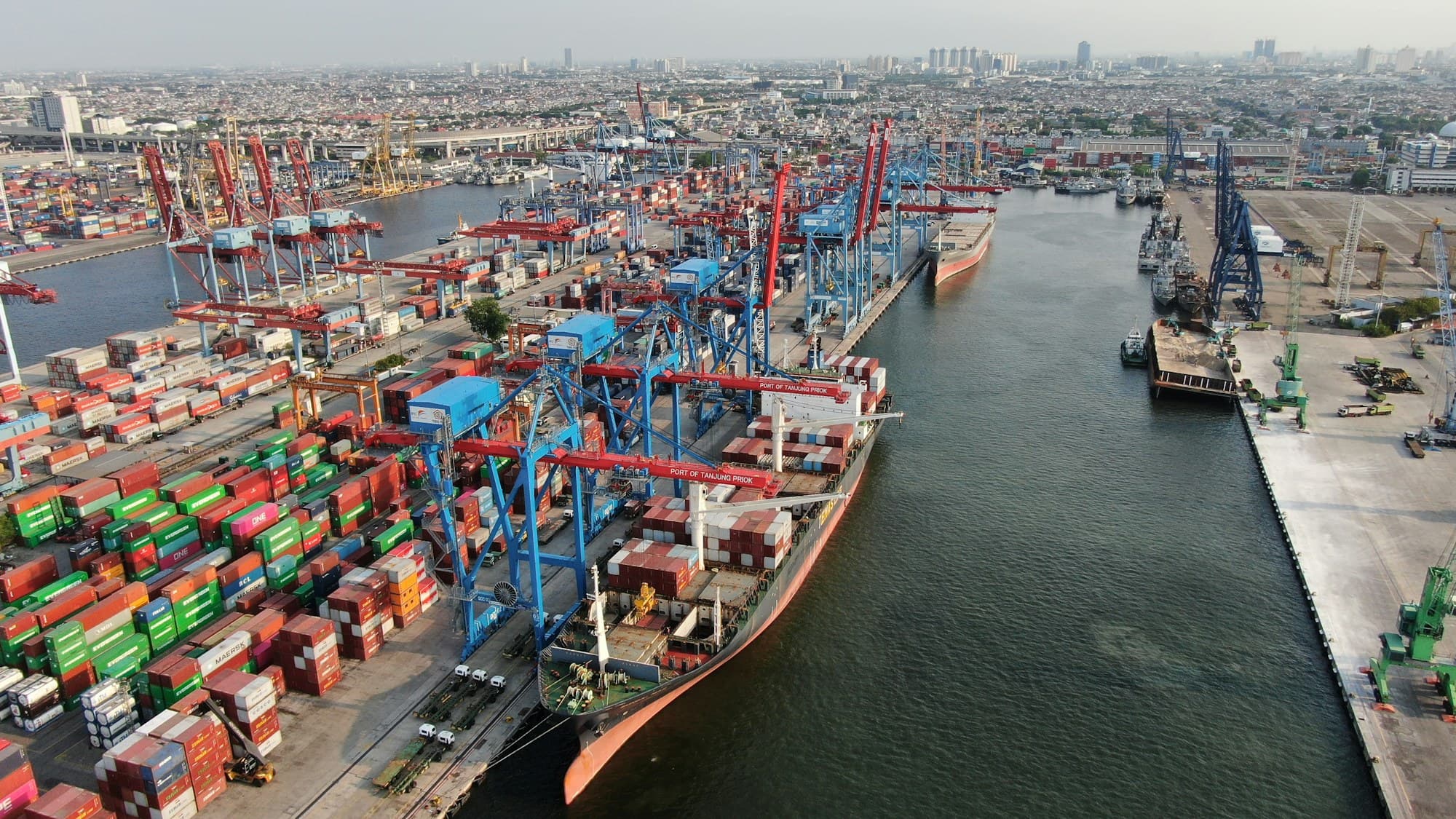 Aerial view of a container terminal, with ship-to-shore cranes loading a vessel alongside stacked freight containers.